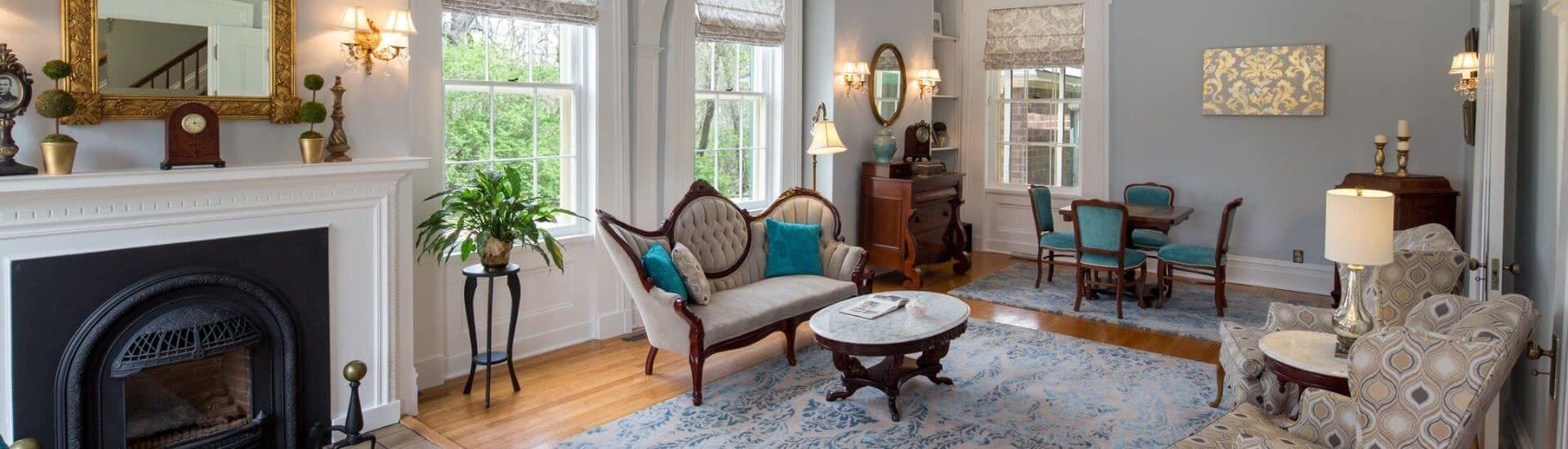 A cozy, elegantly furnished living room with a fireplace, large windows, and a mix of vintage and modern decor.