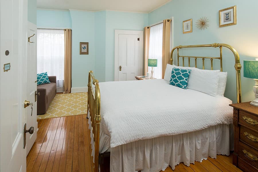 A cozy bedroom with a gold metal bed, light blue walls, and a small seating area.