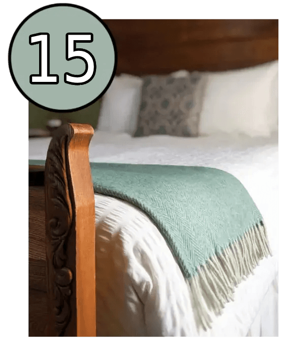 A close-up of a wooden bed frame with a green blanket draped over white bedding.