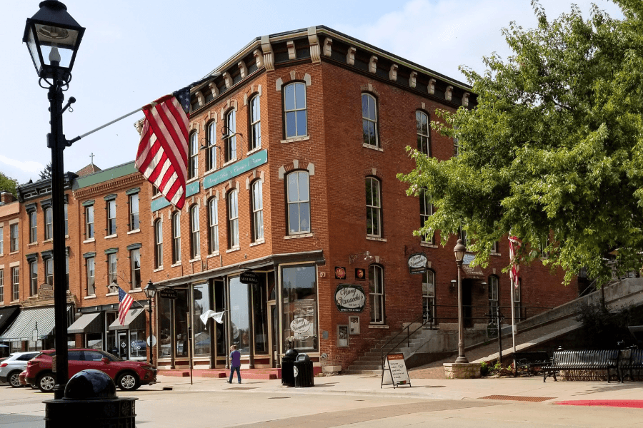 A historic brick building with large windows, an American flag, and a nearby streetlamp in a small town setting.