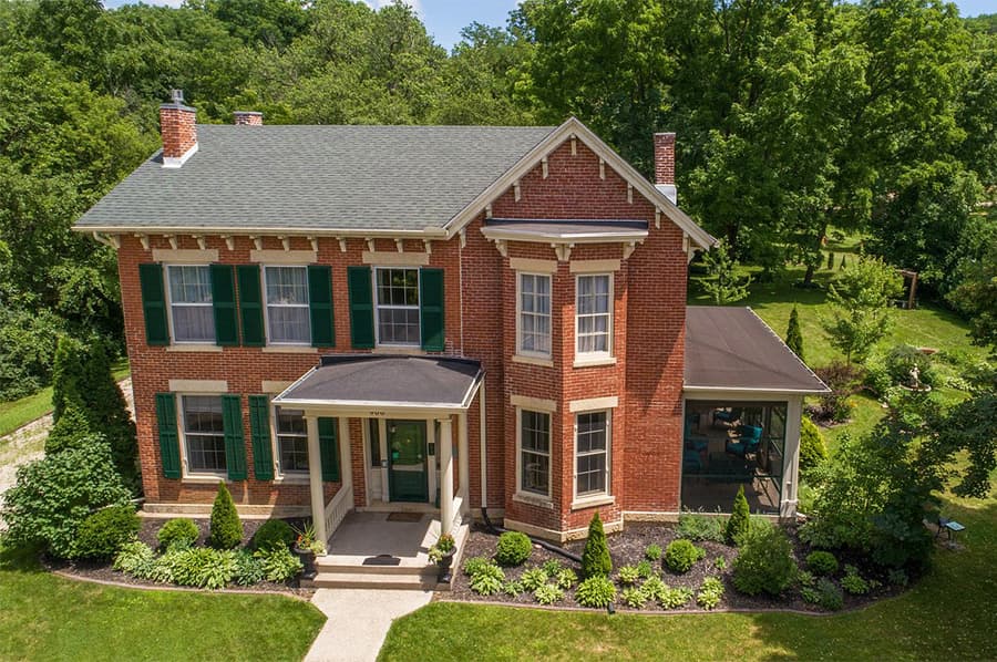 Aerial view of a two-story brick house with green shutters and a landscaped yard.