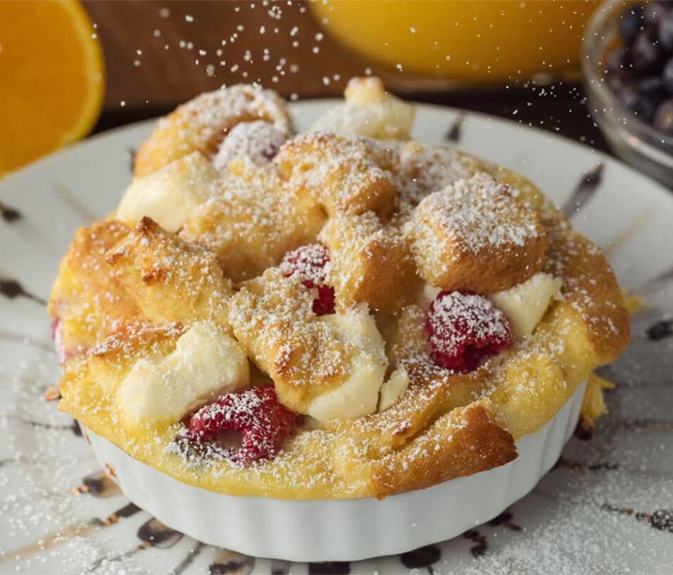 A baked dessert with bread, raspberries, and powdered sugar, served in a white dish.