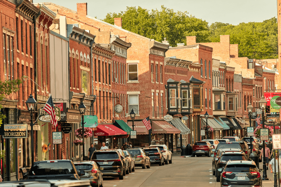 A charming street lined with historic brick buildings and shops, bustling with pedestrians and parked cars.